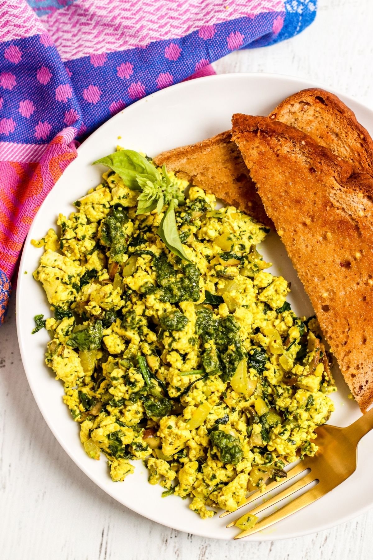 Overhead of plate with pesto scrambled tofu and toast with gold fork and purple napkin.