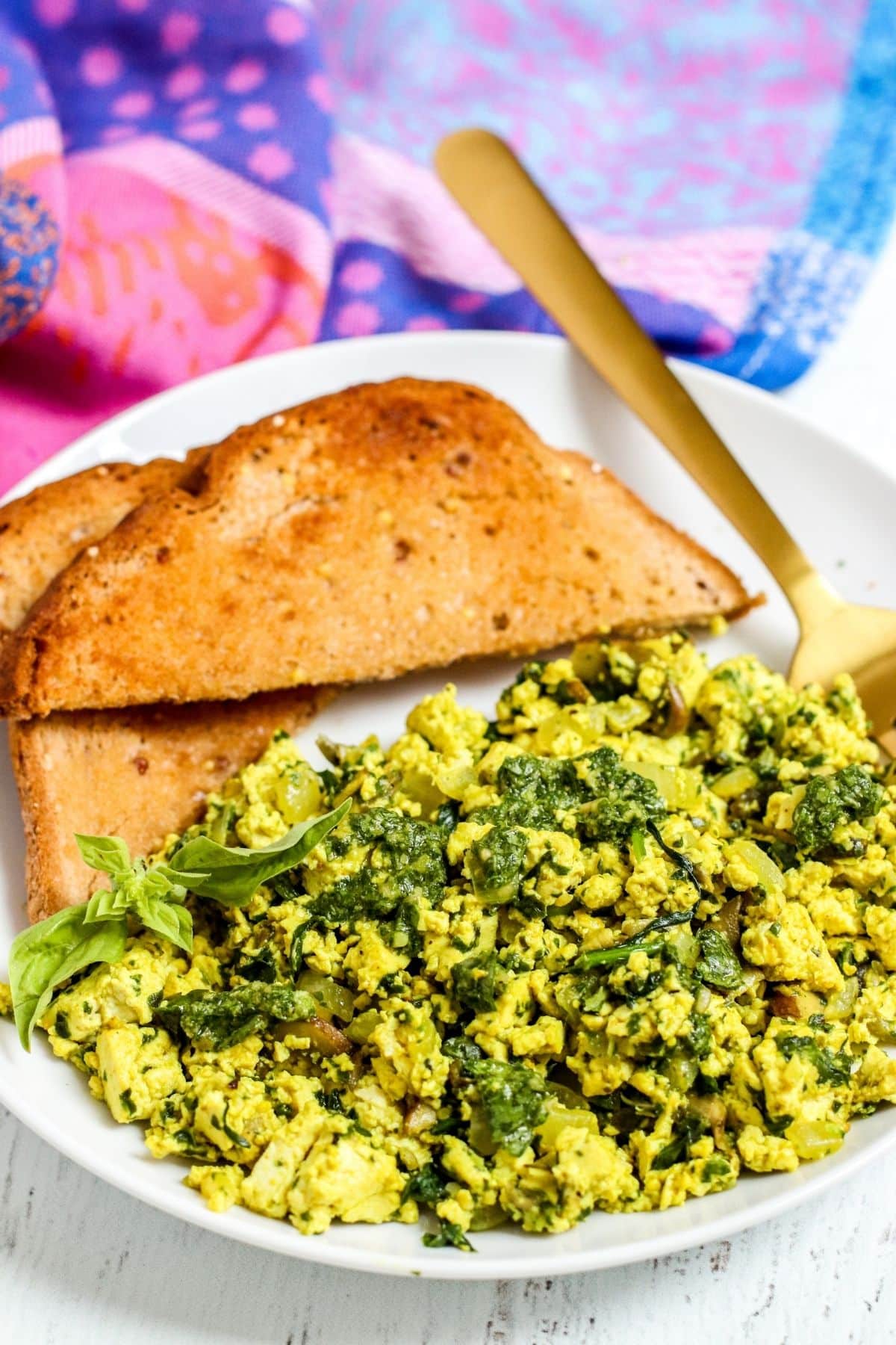 Close up image of finished scrambled tofu topped with pesto with toast on the side.