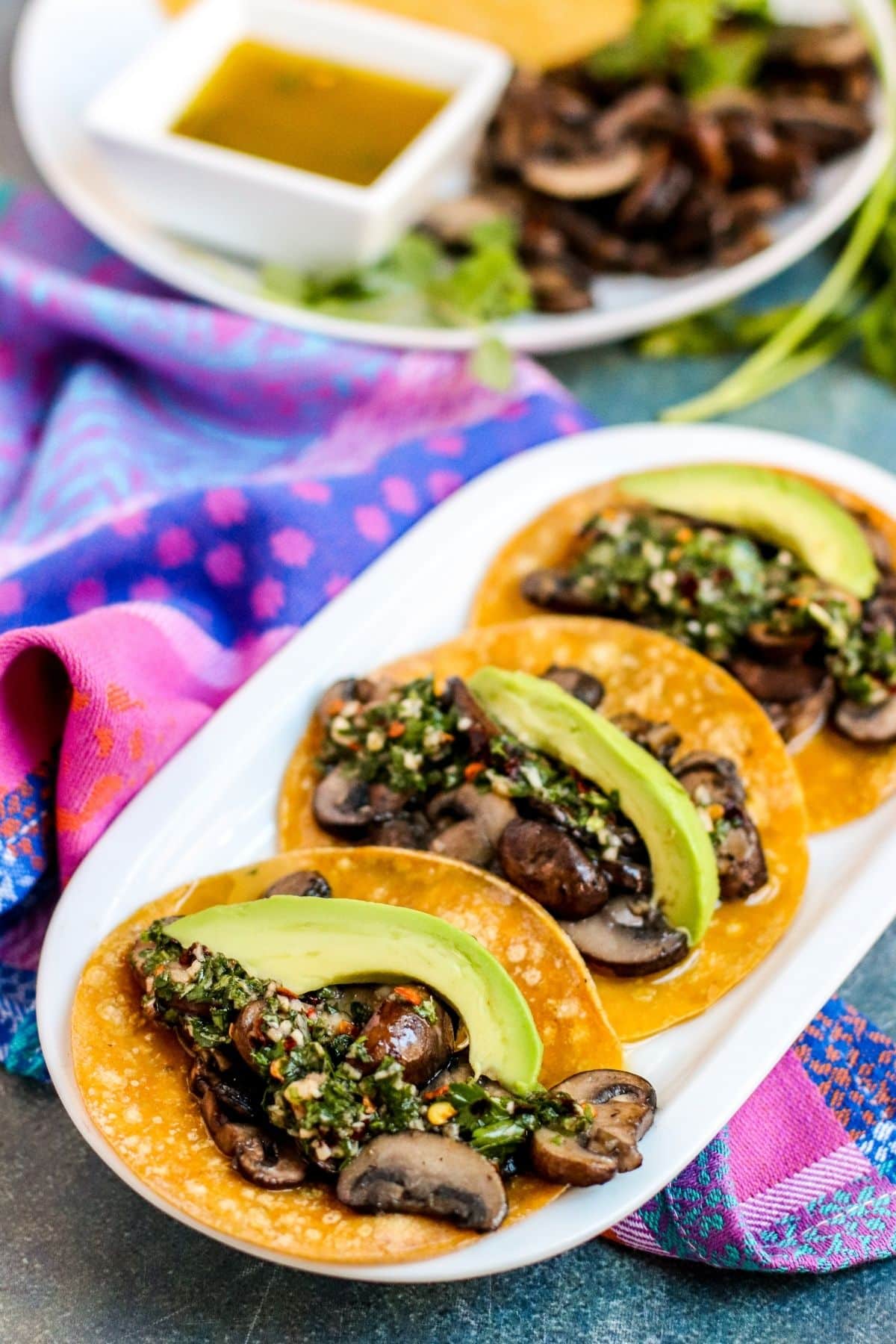 Platter of mushroom tacos topped with herb sauce and avocado slices