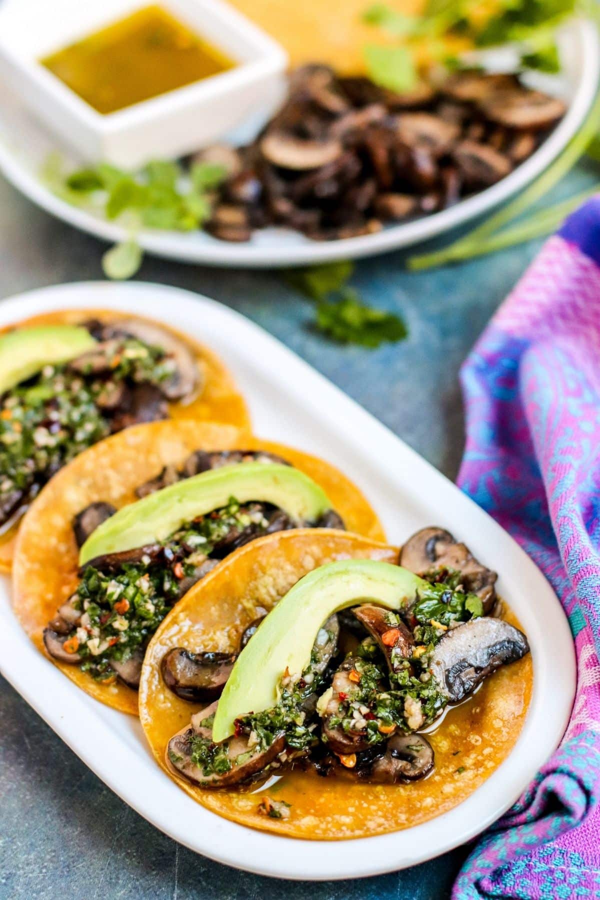 Plater of mushroom tacos topped with avocado slices and Chimichurri sauce