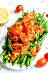 Platter of green beans topped with garlicky tomatoes and pine nuts.