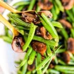 Serving spoons holding green beans and mushrooms above the serving bowl.