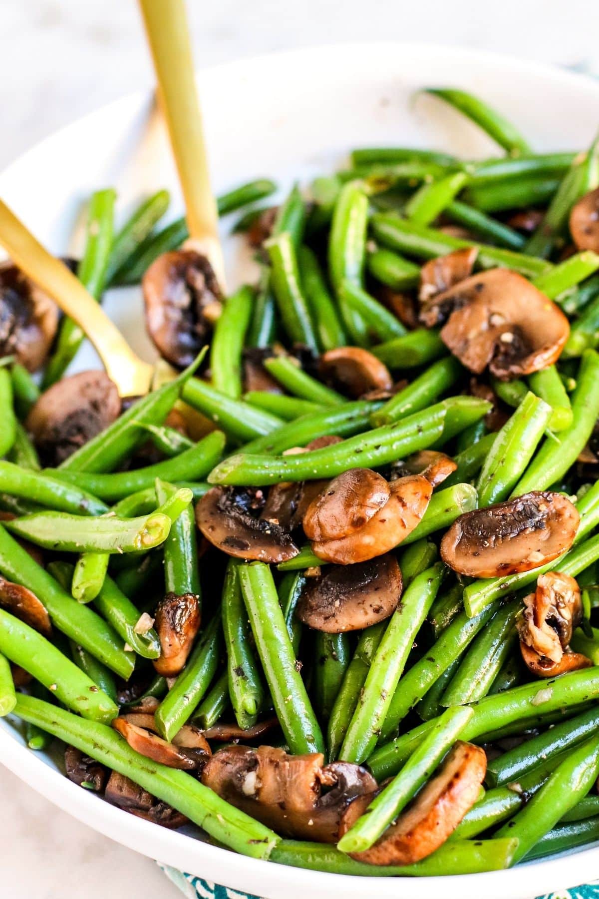 Bowl of green beans and mushrooms with gold serving utensils