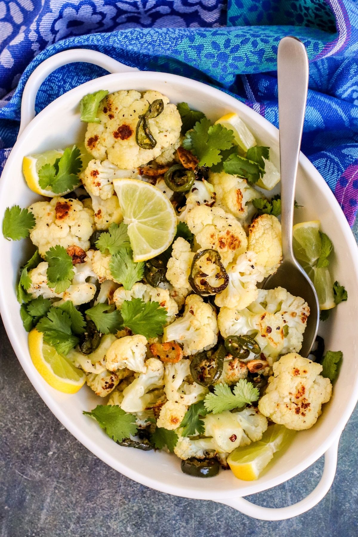 Serving bowl of spicy roasted cauliflower garnished with slices of lime and fresh cilantro