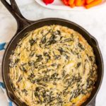 Spinach Artichoke Dip in a cast iron skillet with a platter of raw vegetables.