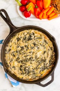 Spinach Artichoke Dip in a cast iron skillet with a platter of raw vegetables.