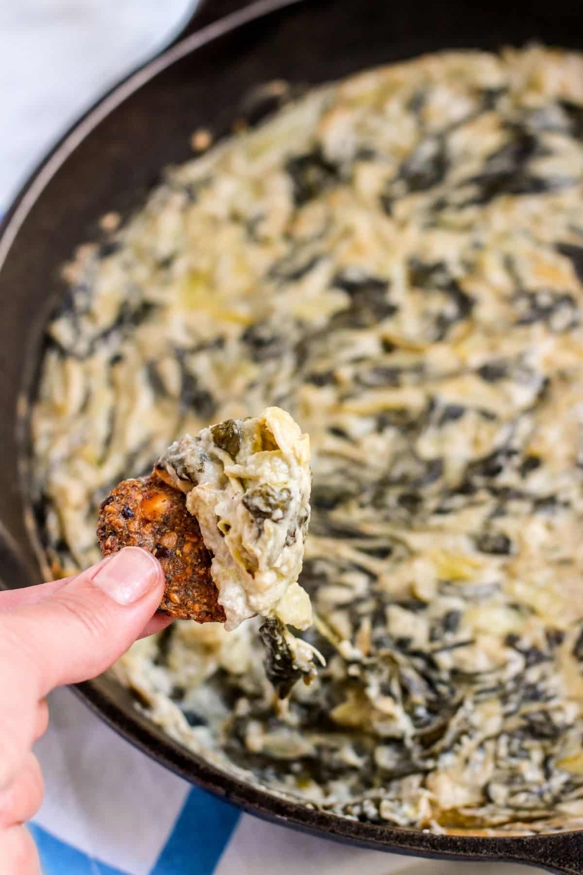 Hand dipping cracker into the skillet of dip