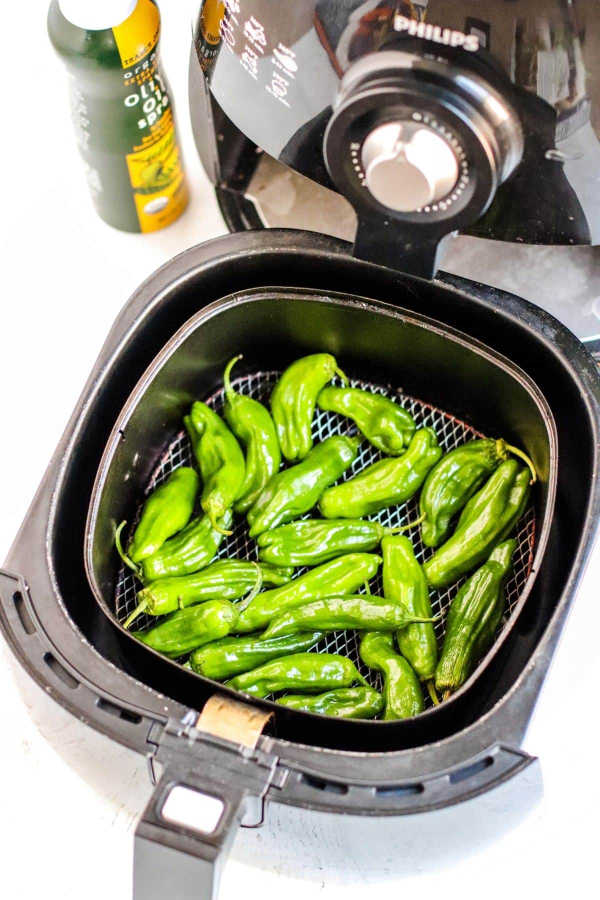 Pepper in an air fryer basket with bottle of olive oil spray next to it