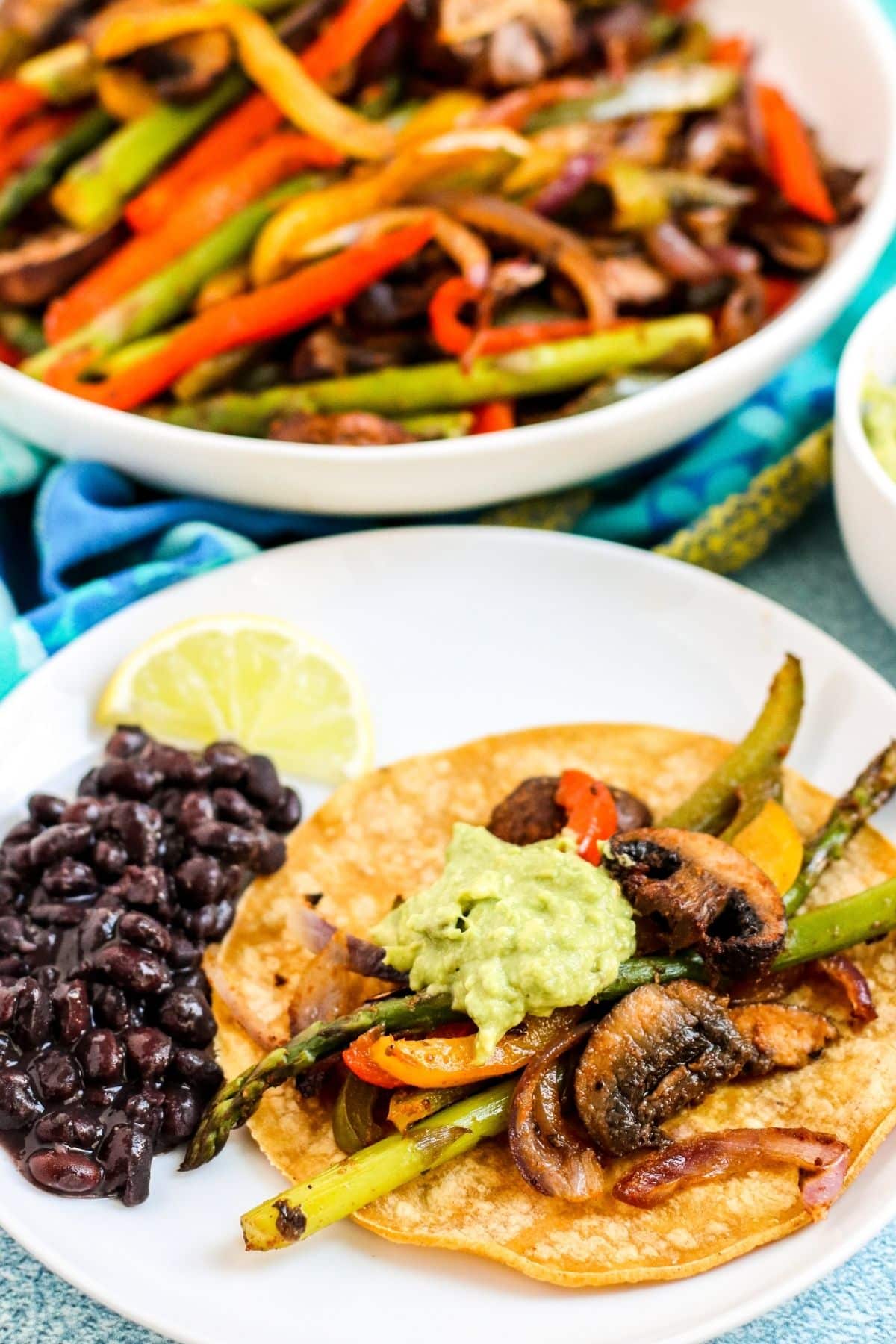 Plate with fajitas on a corn tortilla topped with guacamole and a side of black beans