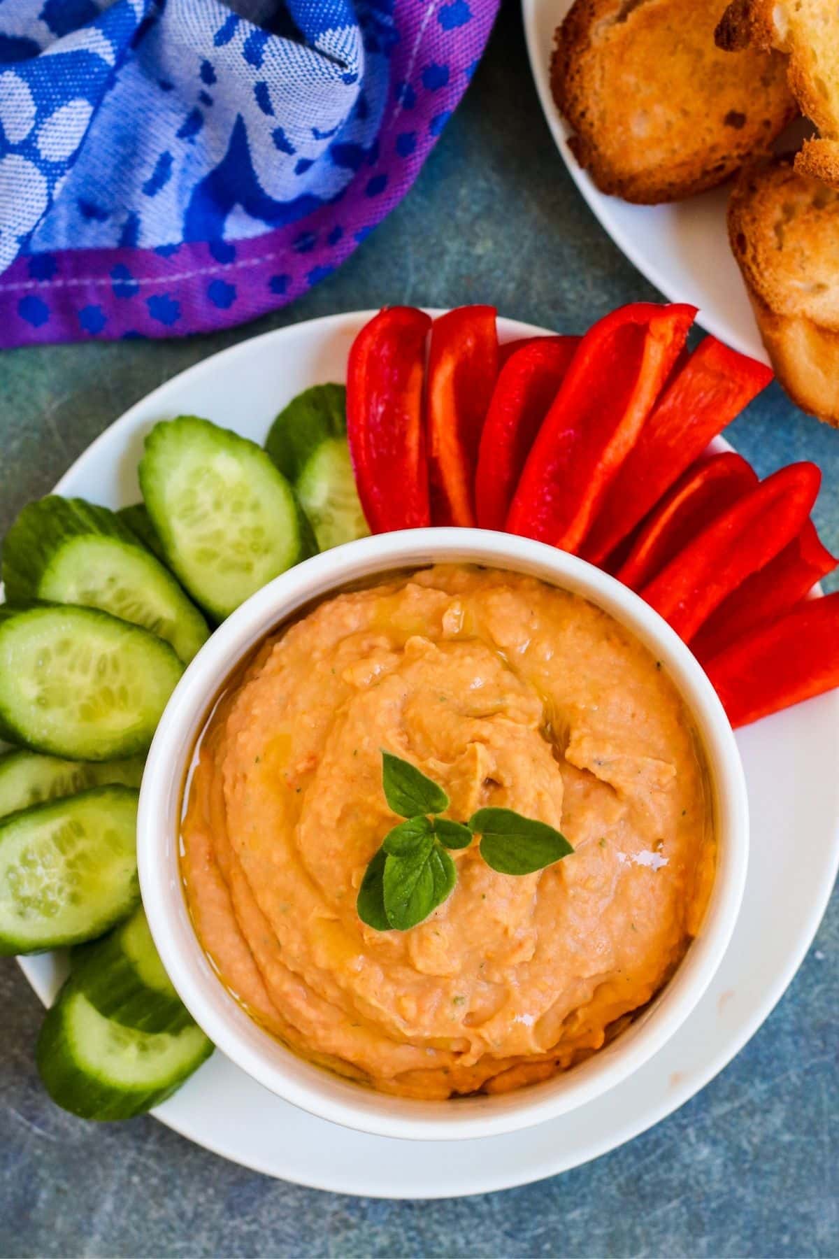 Plate with cucumber slices and strips of red bell pepper around a bowl of sun-dried tomato dip.