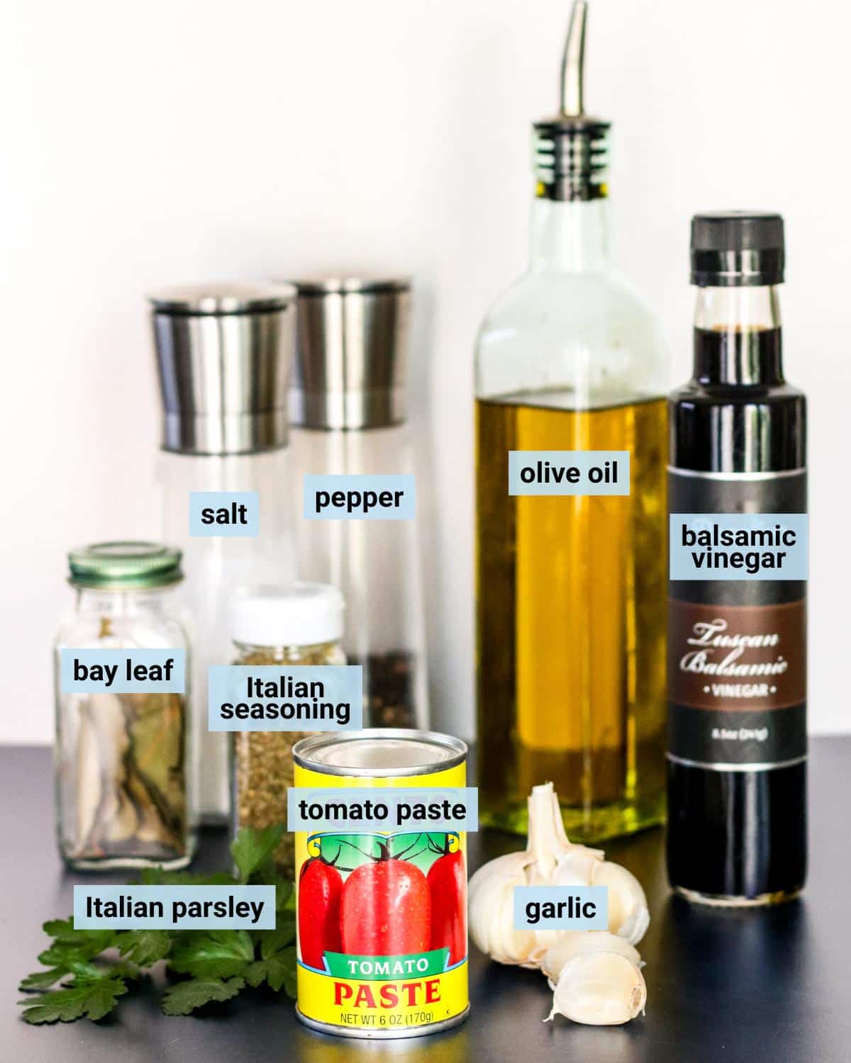 Can of tomato paste, garlic, Italian parsley, jars of bay leaves and Italian seasoning, bottles of olive oil and balsamic vinegar, and salt and pepper grinders.