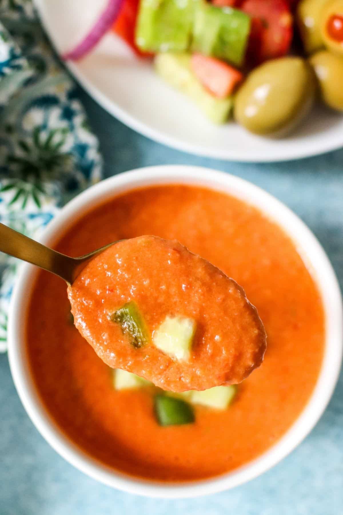 Close up image of gazpacho on a spoon held above a bowl