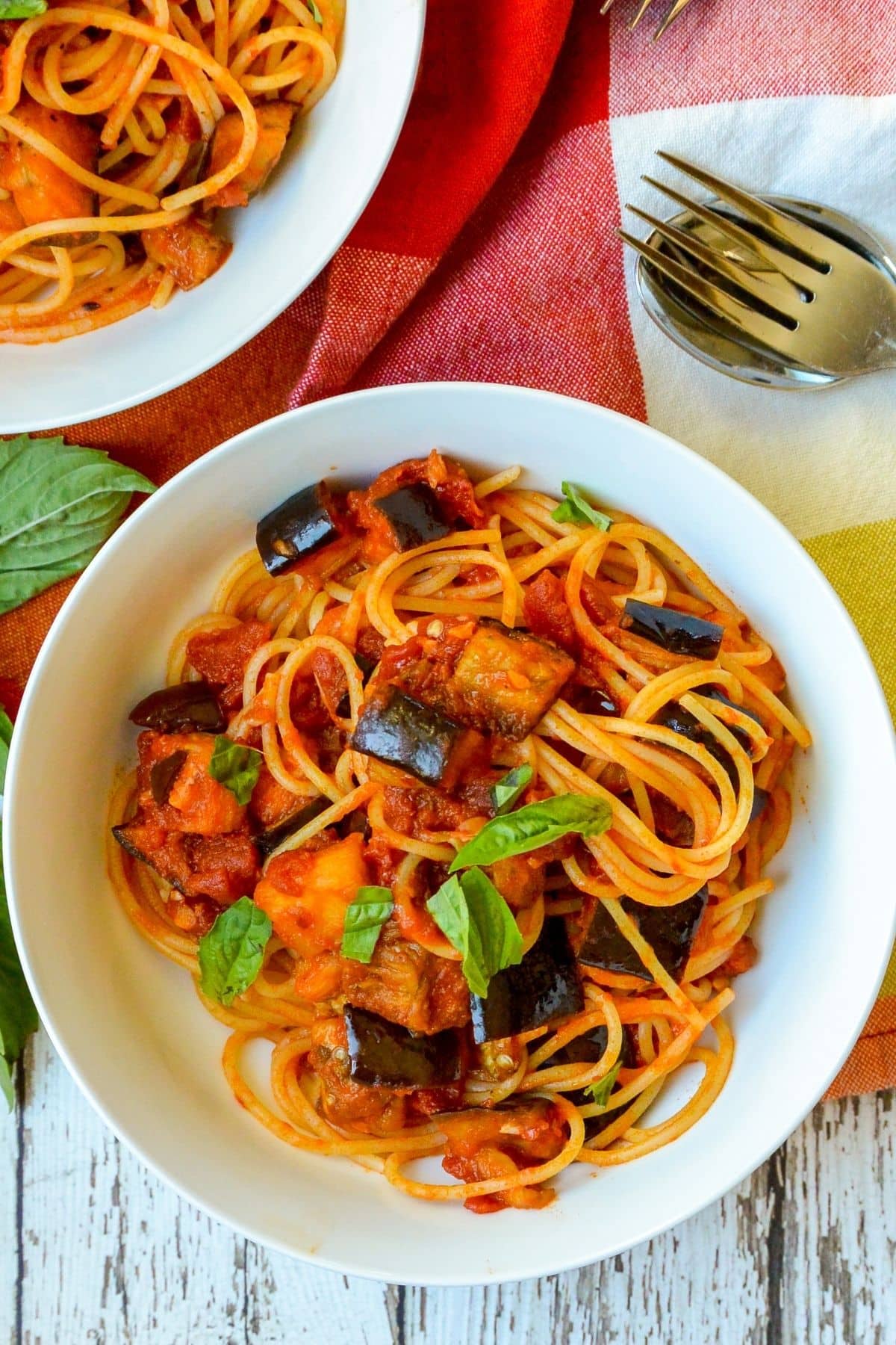 Overhead of bowl of pasta with cubes of eggplant garnished with fresh basil