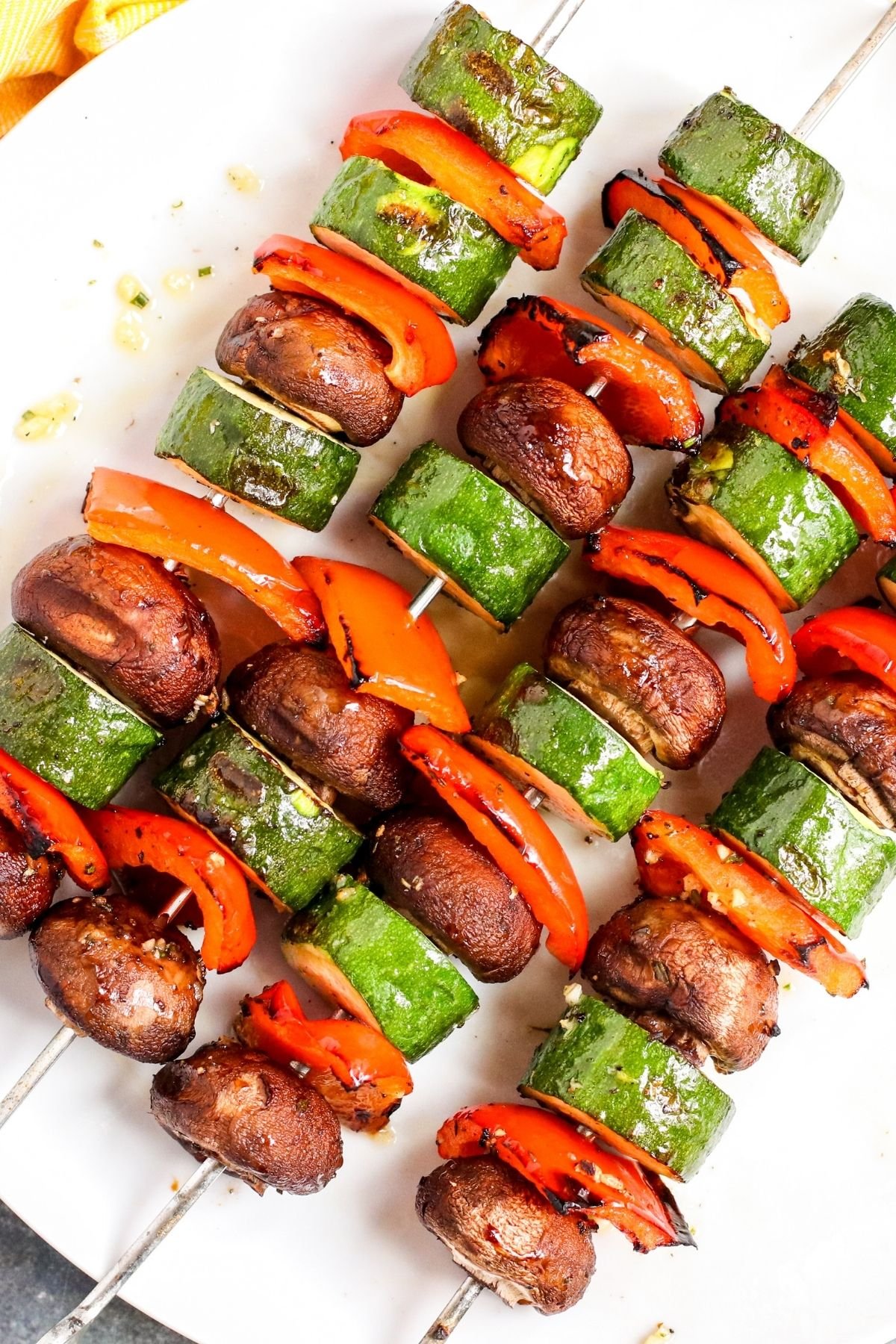 Platter of grilled zucchini, red bell peppers, and mushrooms on metal skewers