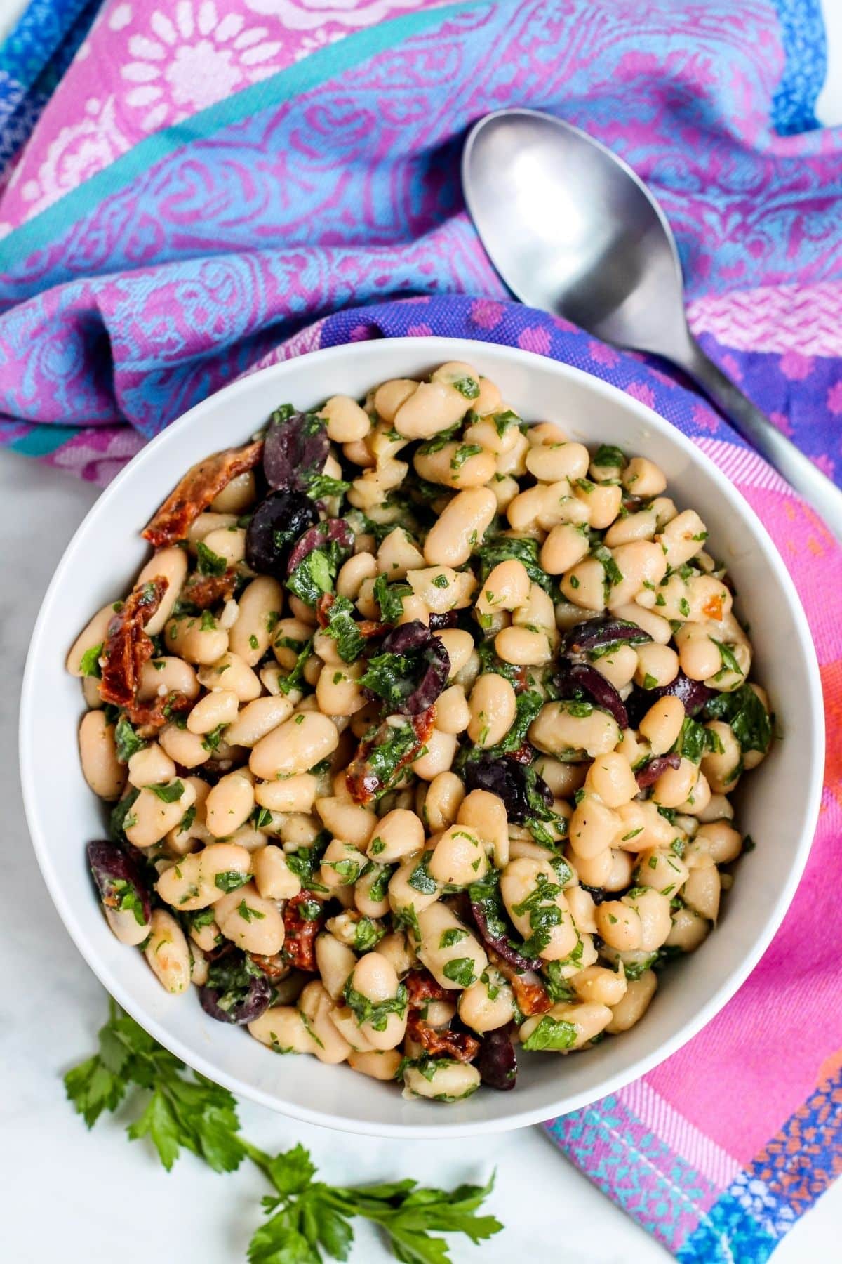 Bowl of salad with white beans, sun-dried tomatoes, olives, and parsley.