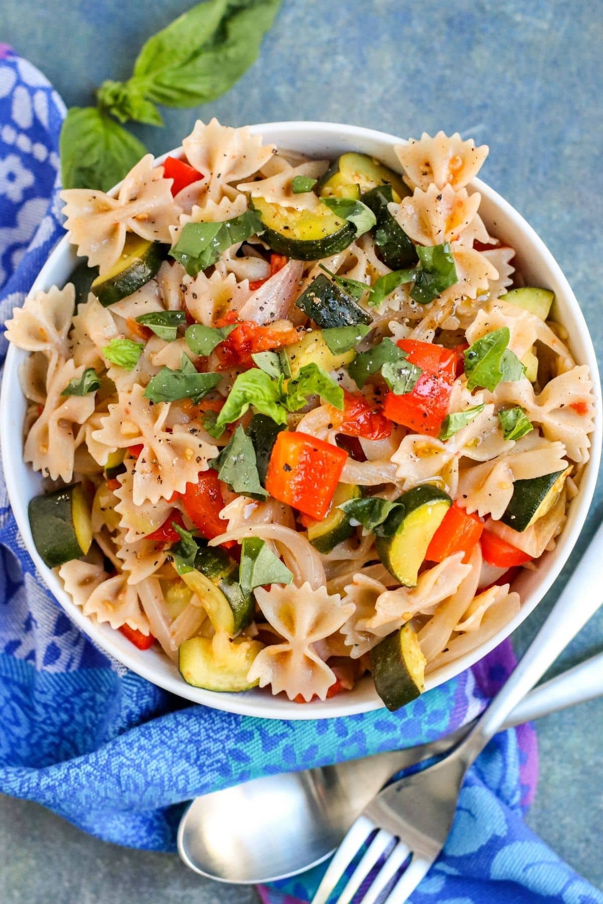 Bowl of bow tie pasta tossed with roasted zucchini, red bell pepper, tomatoes, onion, and fresh basil