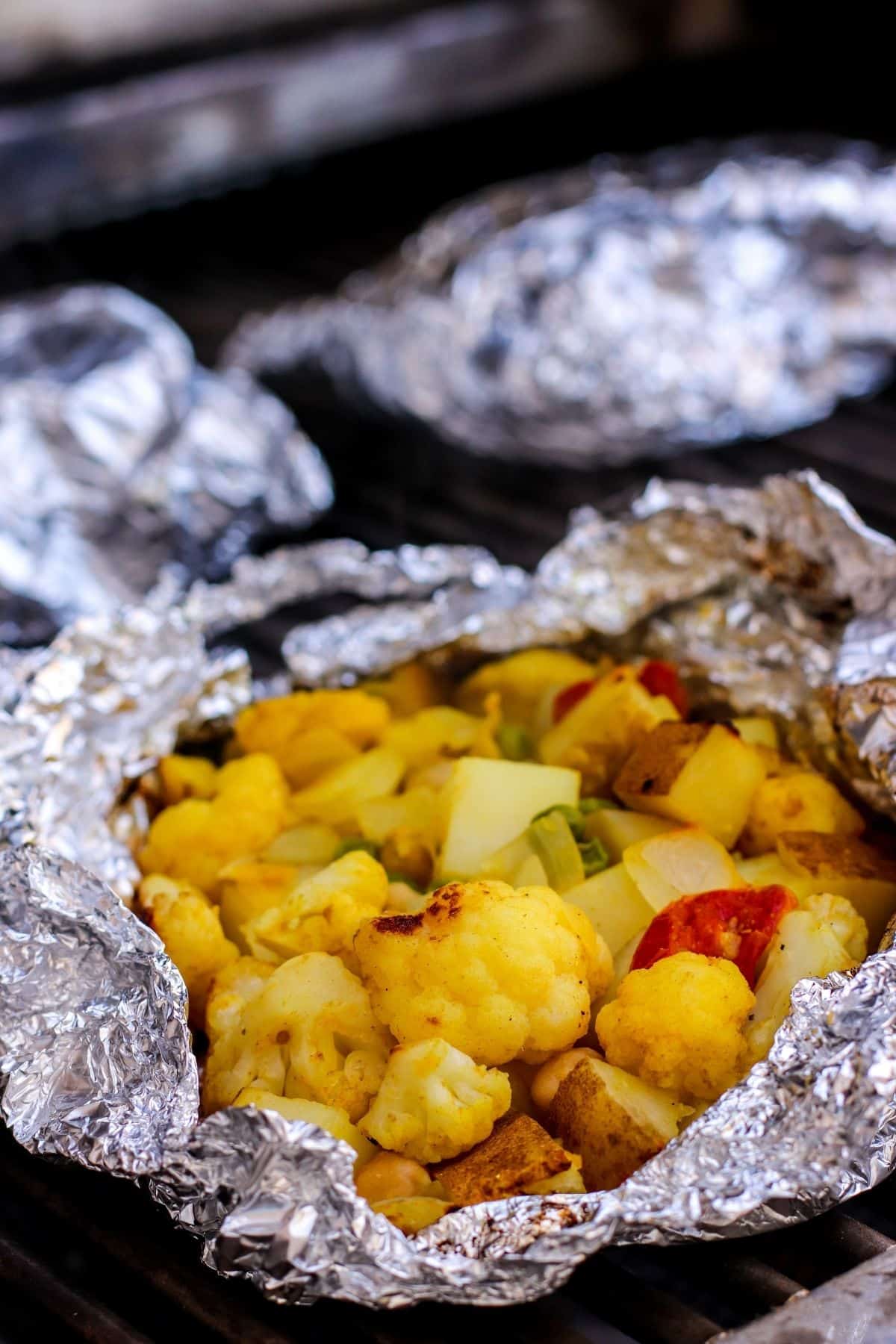 Foil packs on an outdoor grill with the one in front open revealing the cooked contents