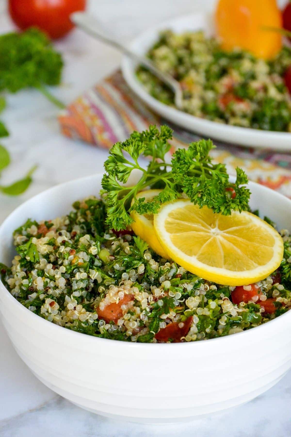Bowl of quinoa tabbouleh garnished with lemon slices and sprig of parsley