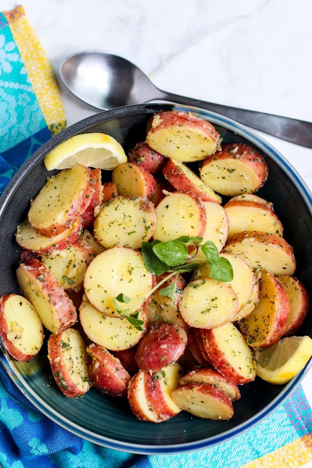 Bowl of Greek potato salad garnished with lemon slices and sprig of oregano