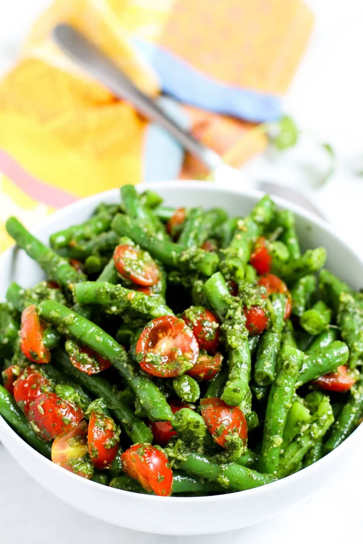 Bowl of green beans salad with cherry tomatoes topped with cilantro sauce