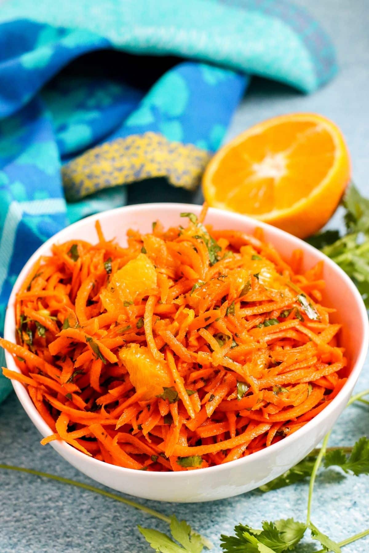 White bowl filled with shredded carrot salad with cut orange in the background