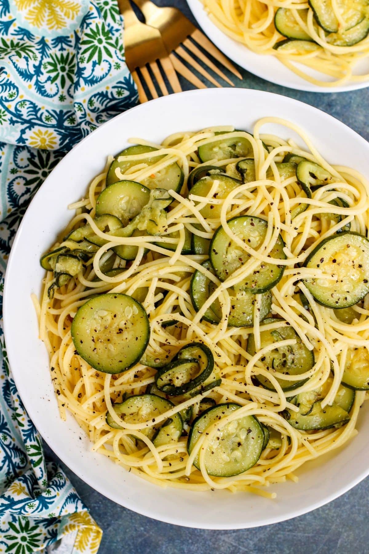 Overhead of a bowl of spaghetti with pan fried zucchini rounds sprinkled with black pepper