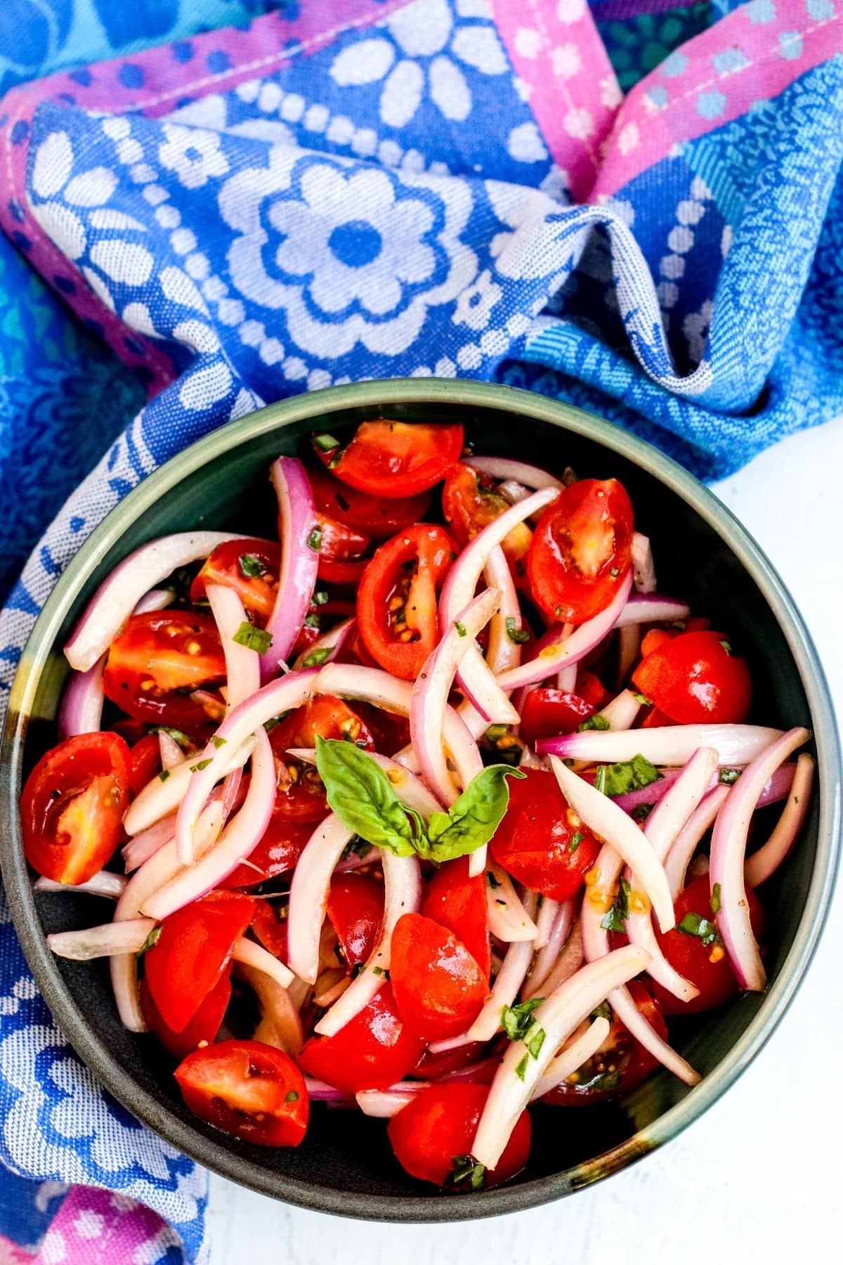 Bowl of tomato and red onion salad next to a purple and blue napkin.