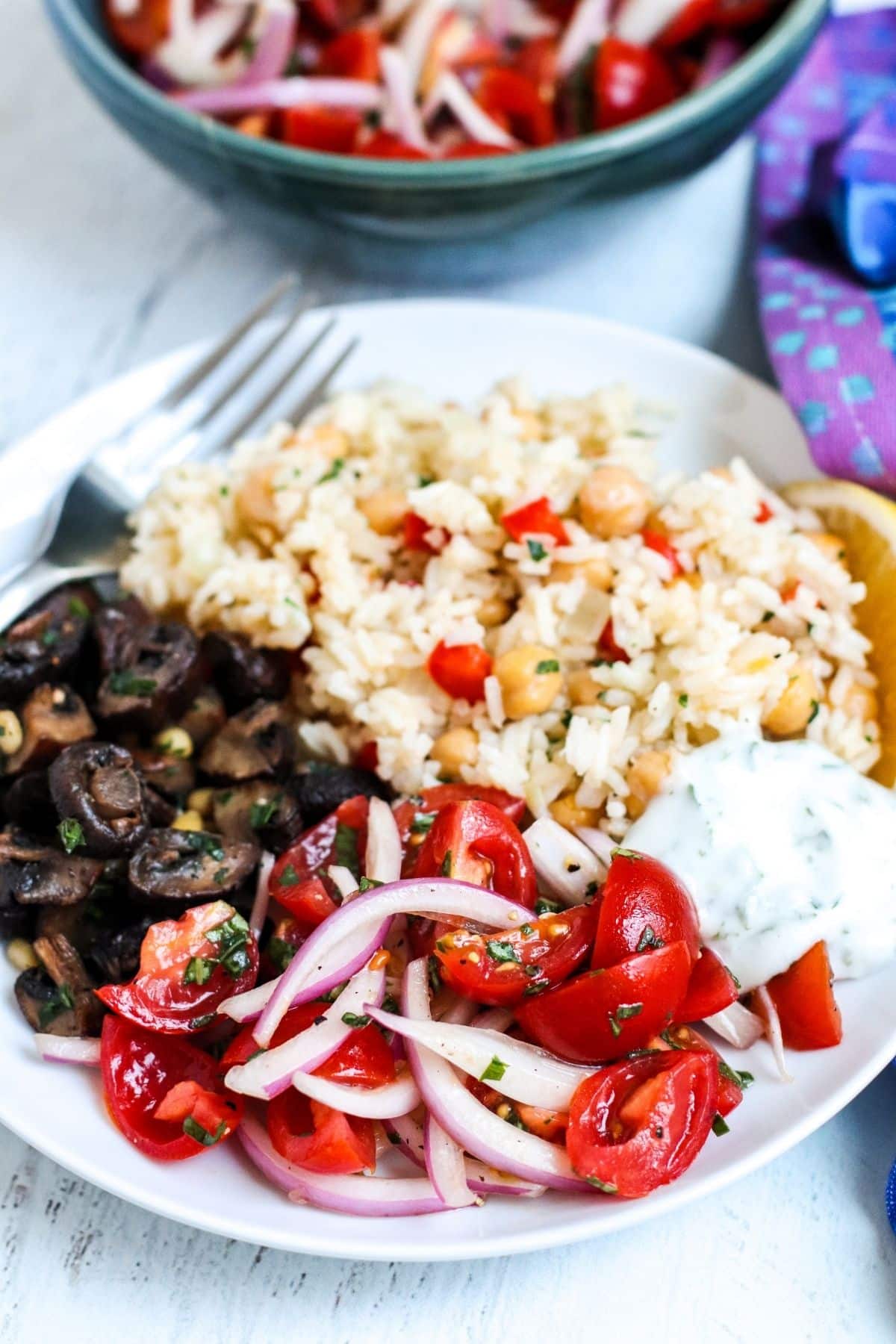 Dinner plate with chickpea rice pilaf, yogurt sauce, tomato and onion salad, and roasted mushrooms.