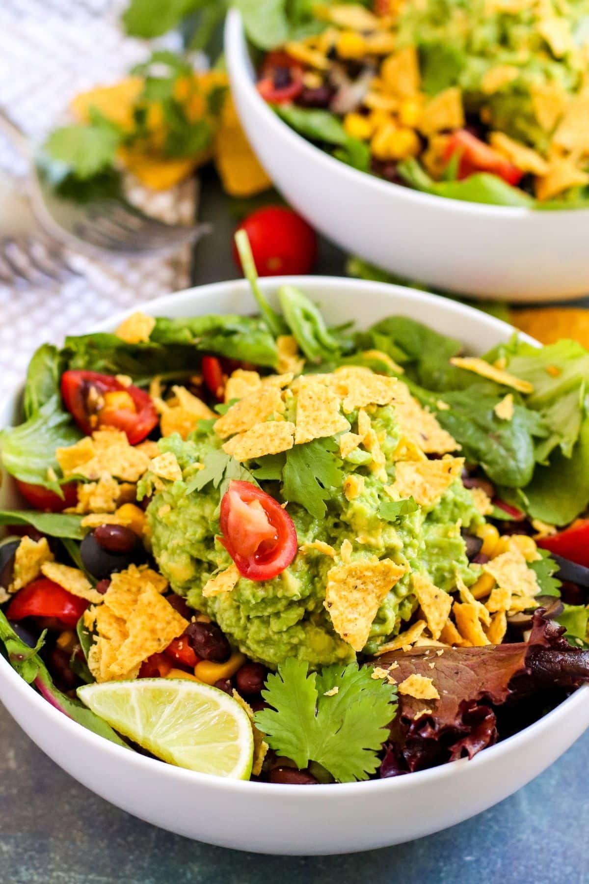 Bowl of salad topped with a big scoop of guacamole and crushed tortilla chips
