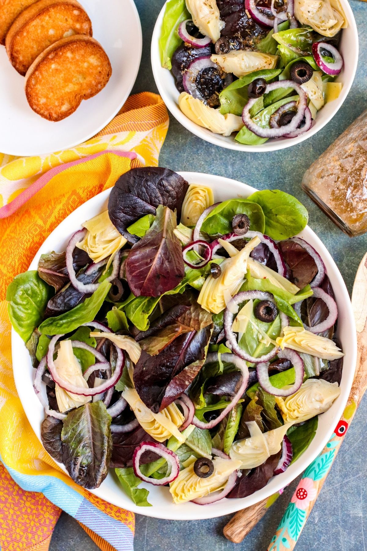 Large serving bowl of mixed greens topped with artichoke hearts, red onions, and black olives.