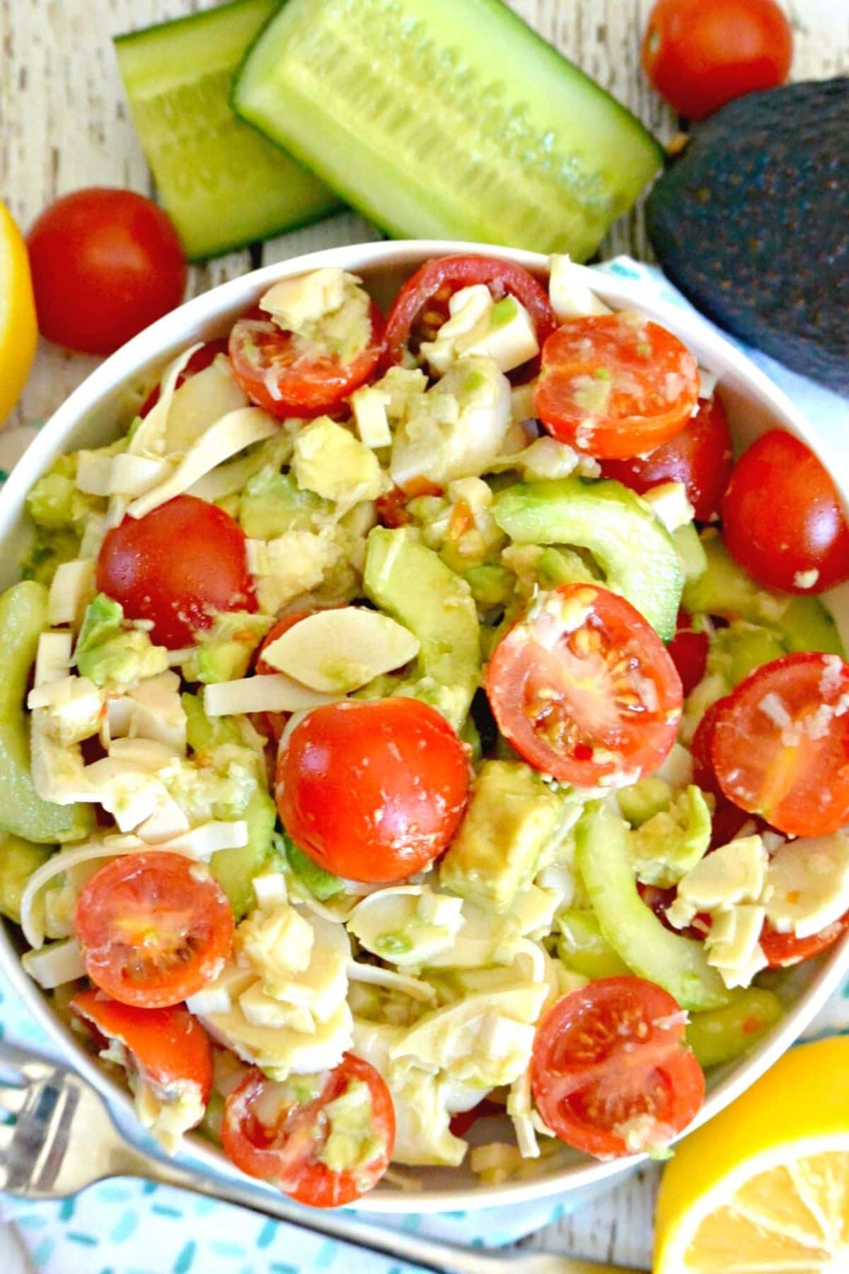 Bowl of Hearts of Palm Salad surrounded by lemons, cucumbers, cherry tomatoes, and an avocado.