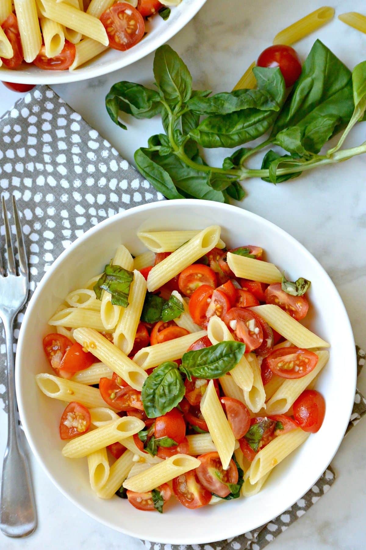 Bowl of penne topped with cherry tomato sauce and sprig of fresh basil