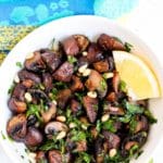 Bowl of roasted mushrooms garnished with a lemon wedge.