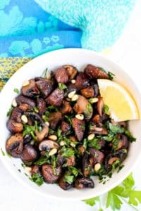 Bowl of roasted mushrooms garnished with a lemon wedge.