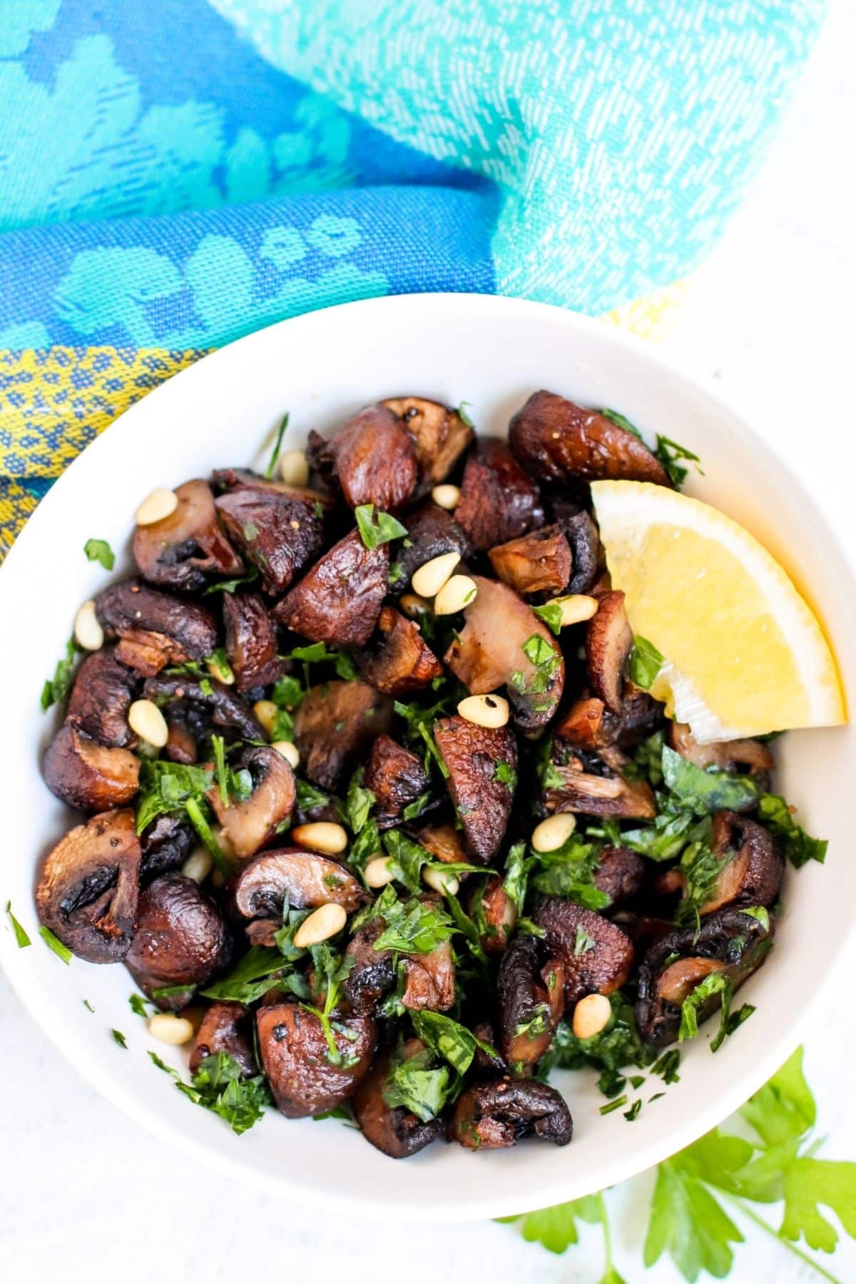 Bowl of roasted baby bella mushrooms topped with pine nuts and chopped parsley.