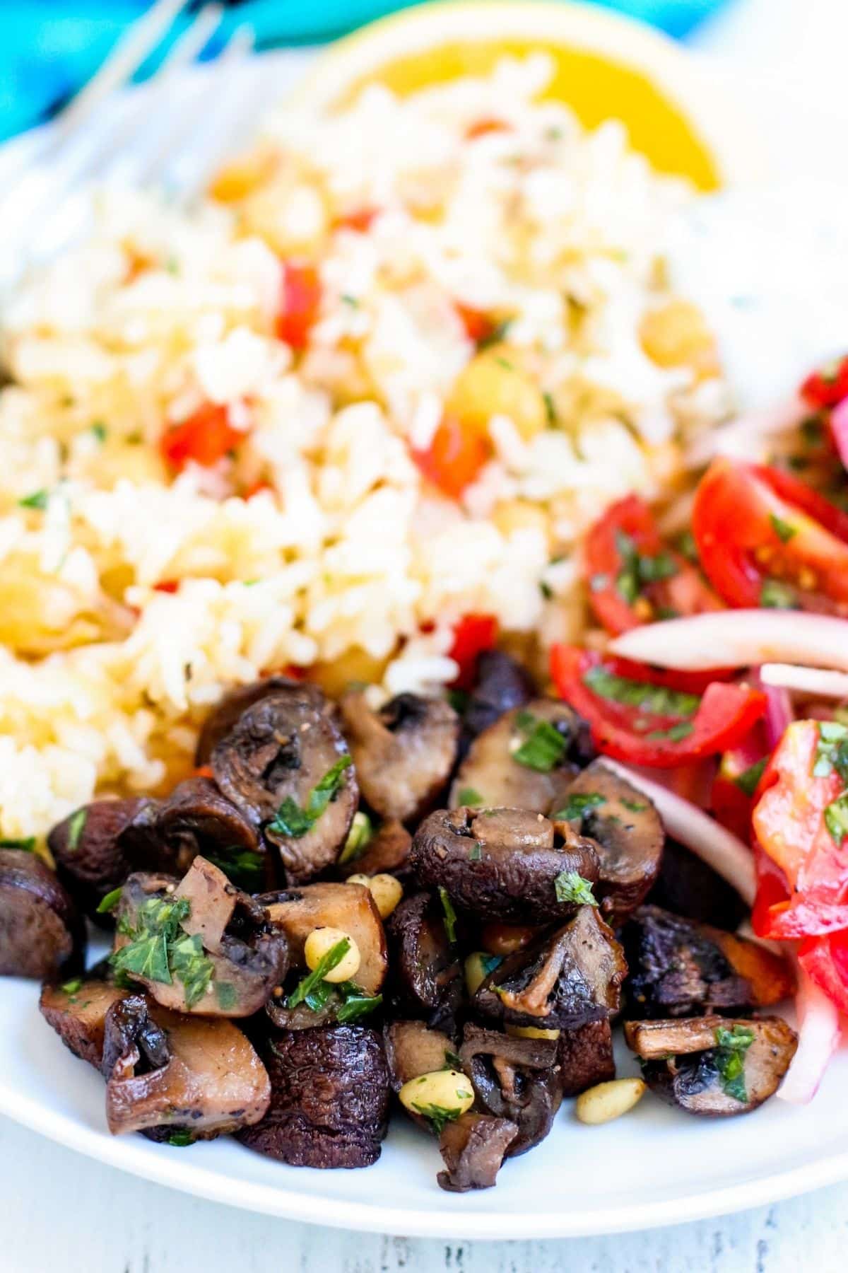 Dinner plate of roasted mushrooms, chickpea rice pilaf, yogurt sauce, and tomatoes and red onions.