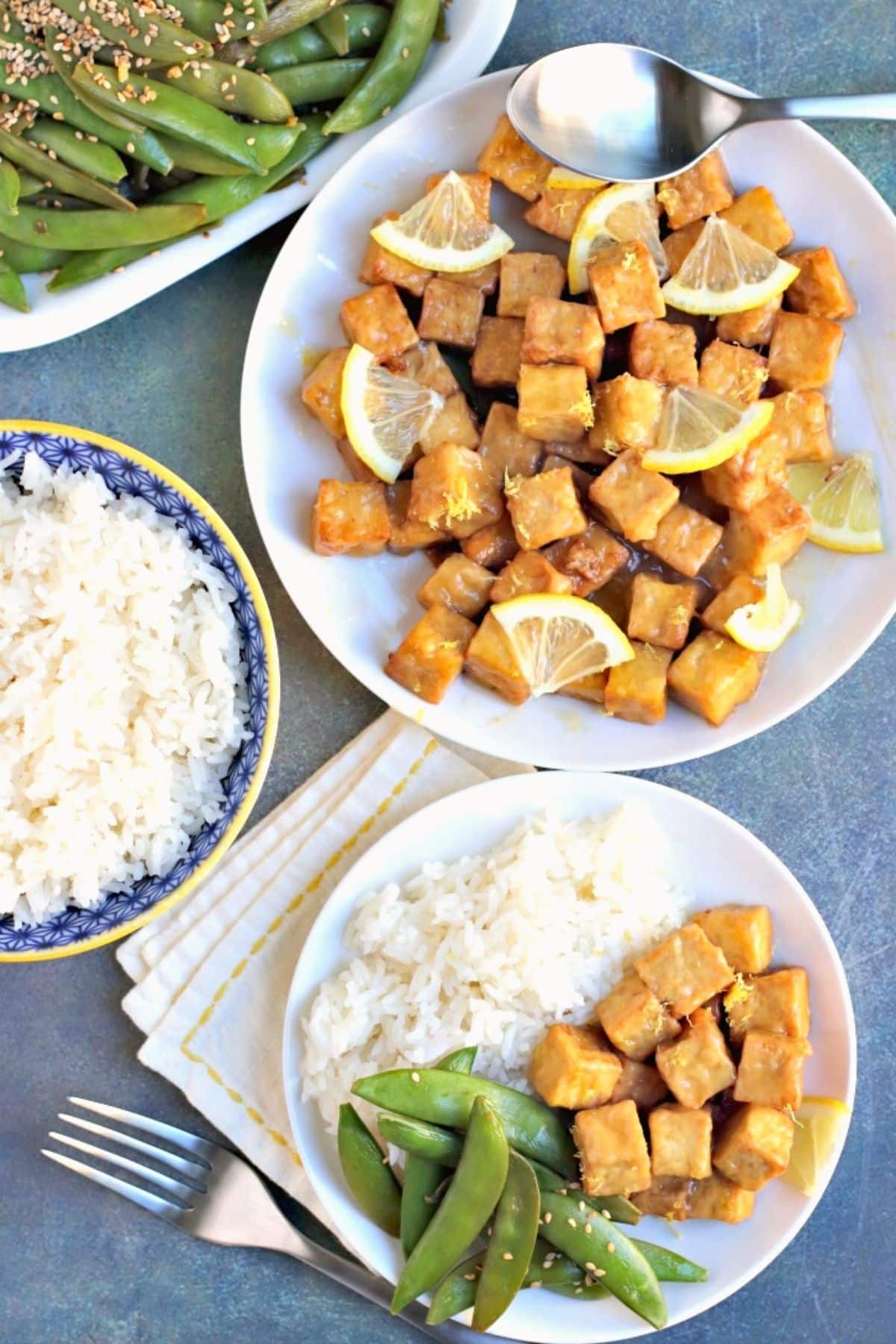 Platter of tofu with lemon sauce, bowl of rice, and dinner plate with rice, tofu, and sugar snap peas