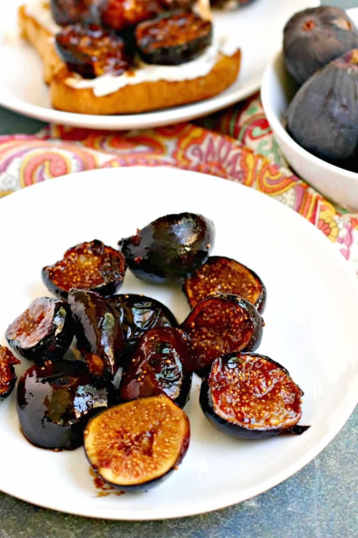 Caramelized figs on a plate with toast and bowl of fresh figs in the background