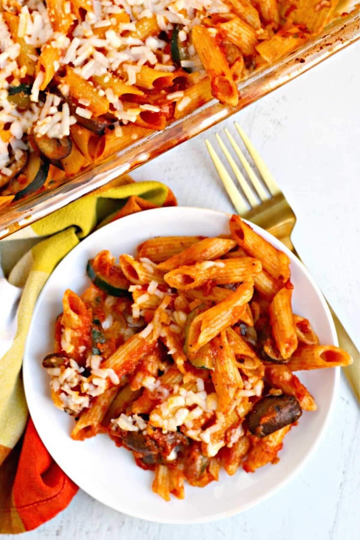 Plate of baked penne pasta with casserole in the background