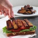Hand placing strip of tofu bacon on a sandwich