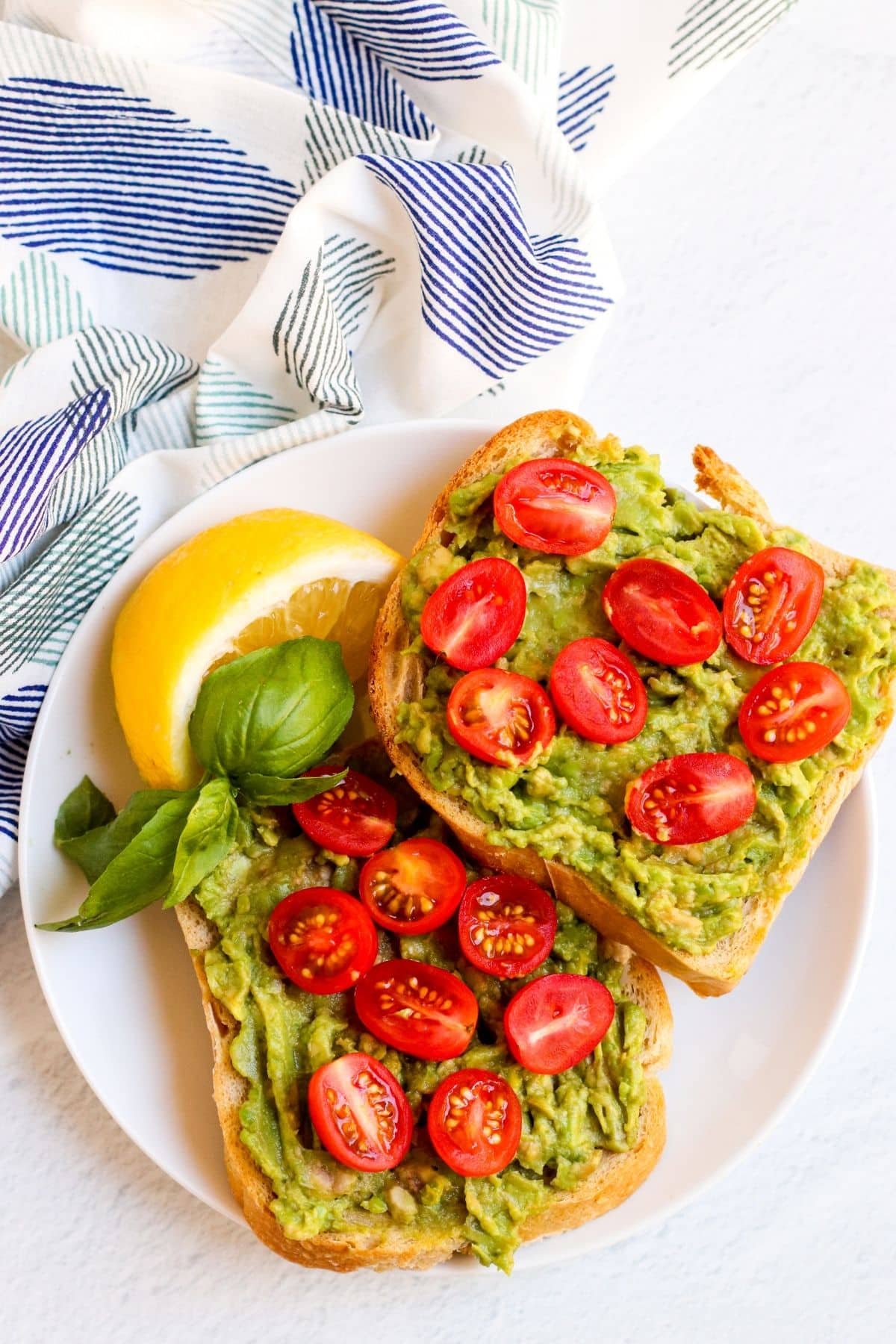 Two slices of avocado toast on a plate topped with halved cherry tomatoes