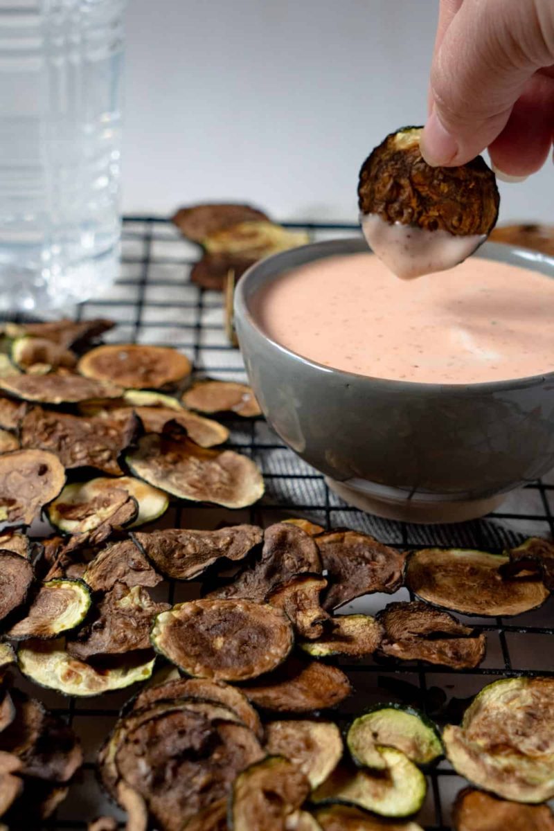 Hand dipping zucchini chip into a bowl of sauce
