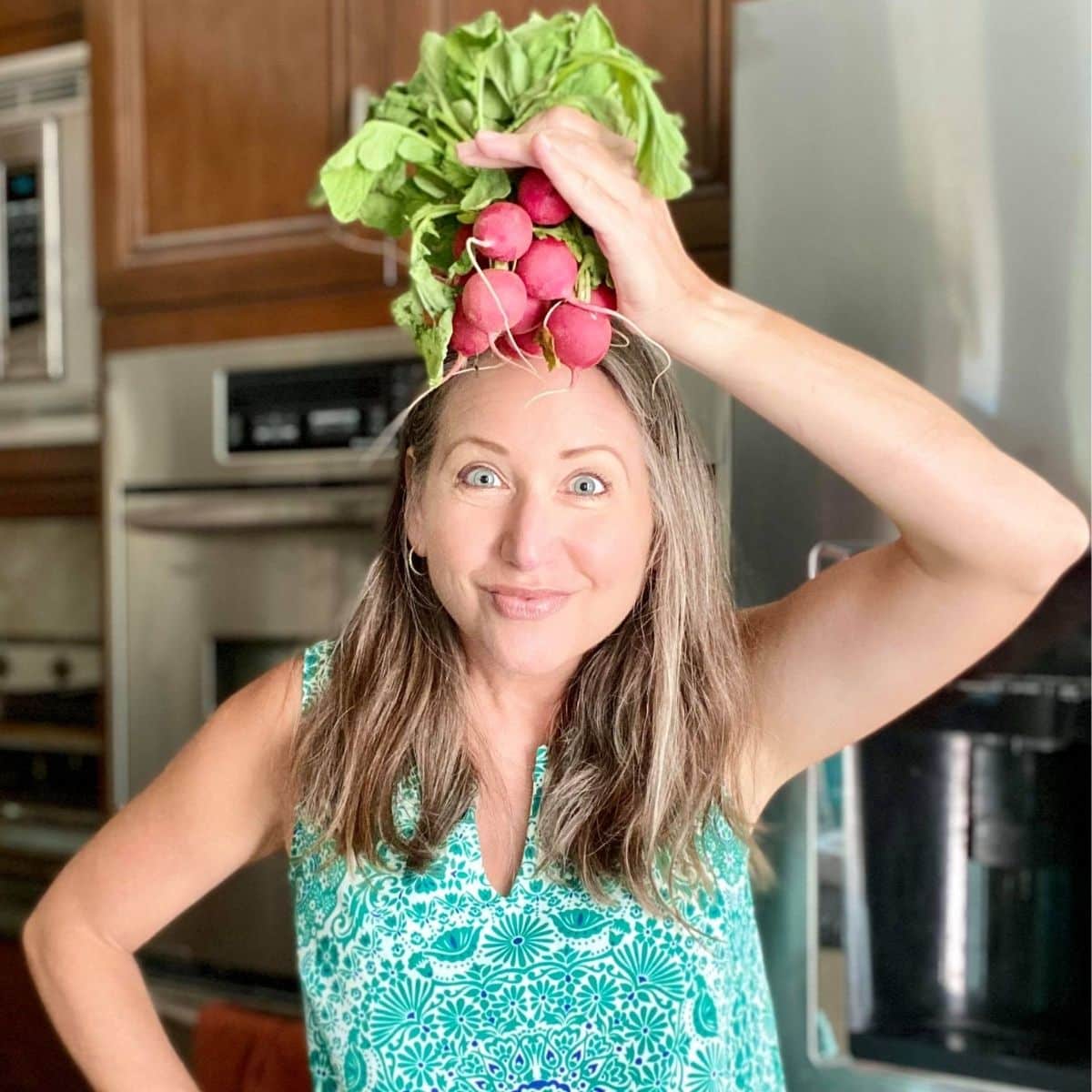 Amy in her kitchen holding a bunch of radishes on her head.