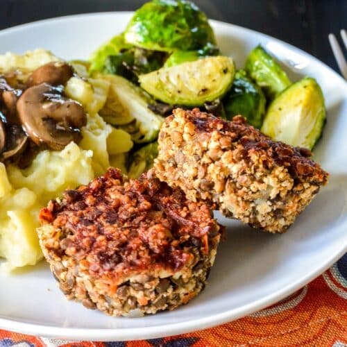 Lentil meatloaf muffins on a plate with mashed potatoes, mushroom gravy, and roasted Brussels sprouts.