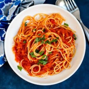 Bowl of spaghetti with pumpkin marinara garnished with fresh parsley next to a fork and blue patterned napkin.