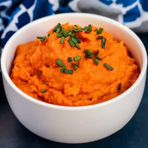 Bowl of mashed sweet potatoes garnished with fresh chopped chives.
