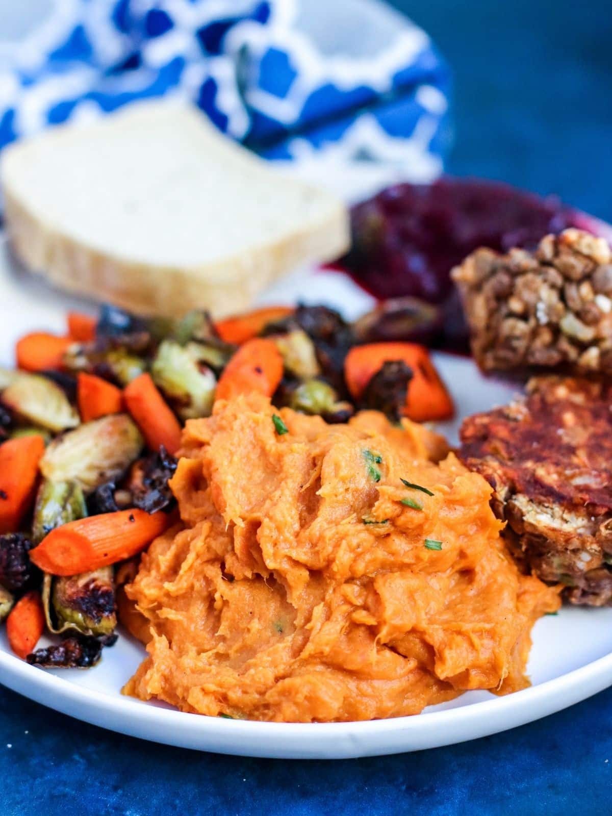 Dinner plate with mashed sweet potatoes, roasted vegetables, bread, cranberry sauce, and lentil meatloaf.