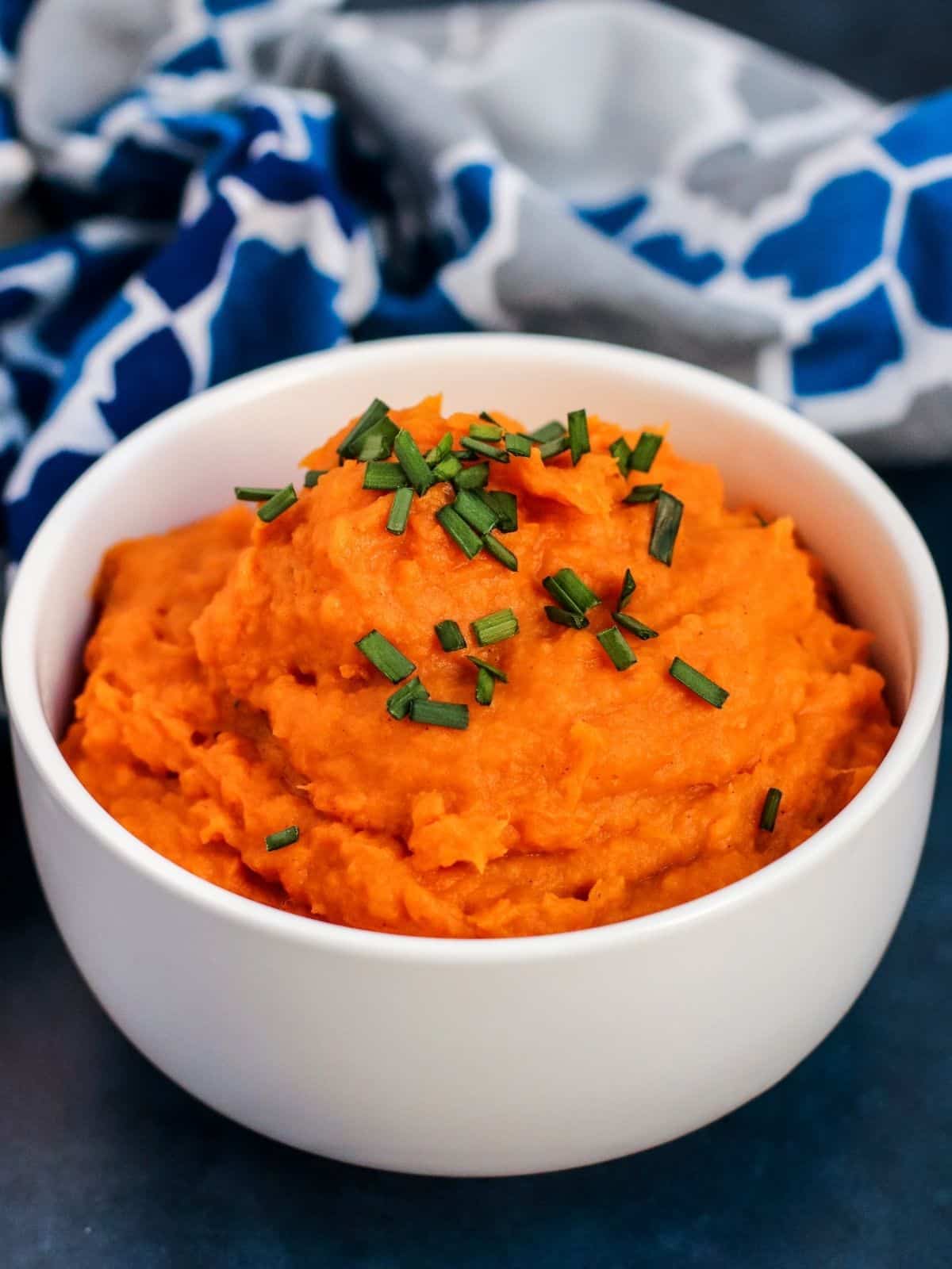 Bowl of mashed sweet potatoes topped with fresh chives next to a blue and white napkin.