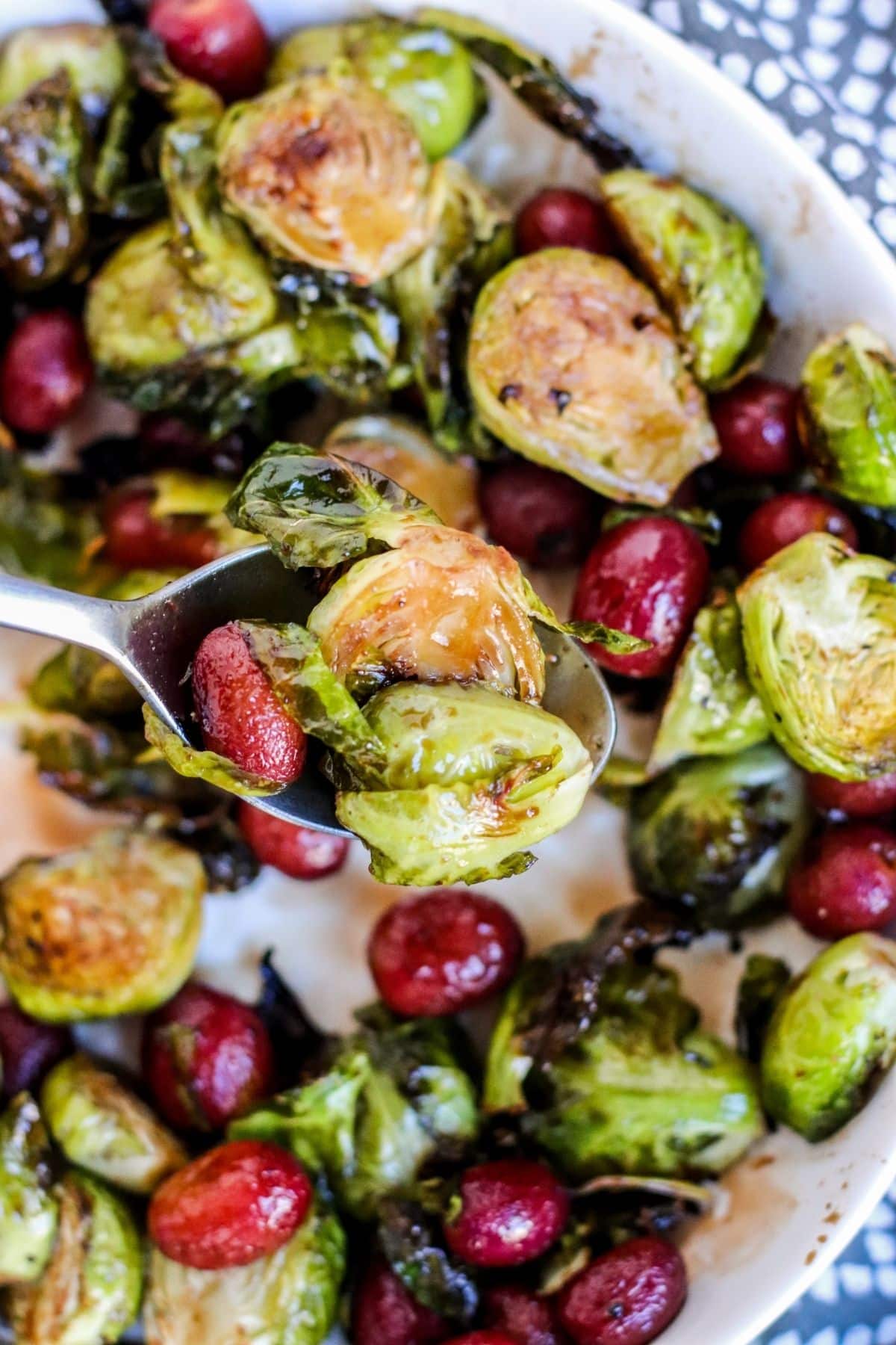 Close up of serving spoon over a platter of roasted grapes and Brussels sprouts.