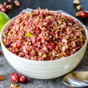 Bowl of relish surrounded by raw cranberries, a green apple, and pecans.